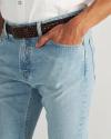 A person wearing light blue jeans, a white shirt, and a brown braided belt stands with one hand in their pocket.