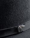 Close-up of a black felt hat with a black ribbon and a silver pin that reads "7 COWS.