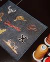 A denim patch with embroidered Western-themed designs and the word “Tecovas,” next to spools of thread on a black surface.