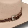 Close-up of a beige felt hat with a brown tooled leather band and a silver buckle detail.