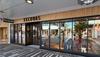 Storefront of Tecovas with large glass windows, wood paneling above, and reflections of nearby shops and street visible outside.