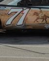 Side view of a race car with the number 71 and an image of a cowboy riding a horse on its door, parked on asphalt.