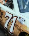 Close-up of a NASCAR race car door showing the number 71 and a NASCAR Cup Series logo, with part of a desert-themed graphic visible.