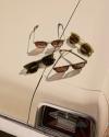 Four pairs of sunglasses with brown lenses are arranged on the cream-colored trunk of a vintage car, near the rear taillight.