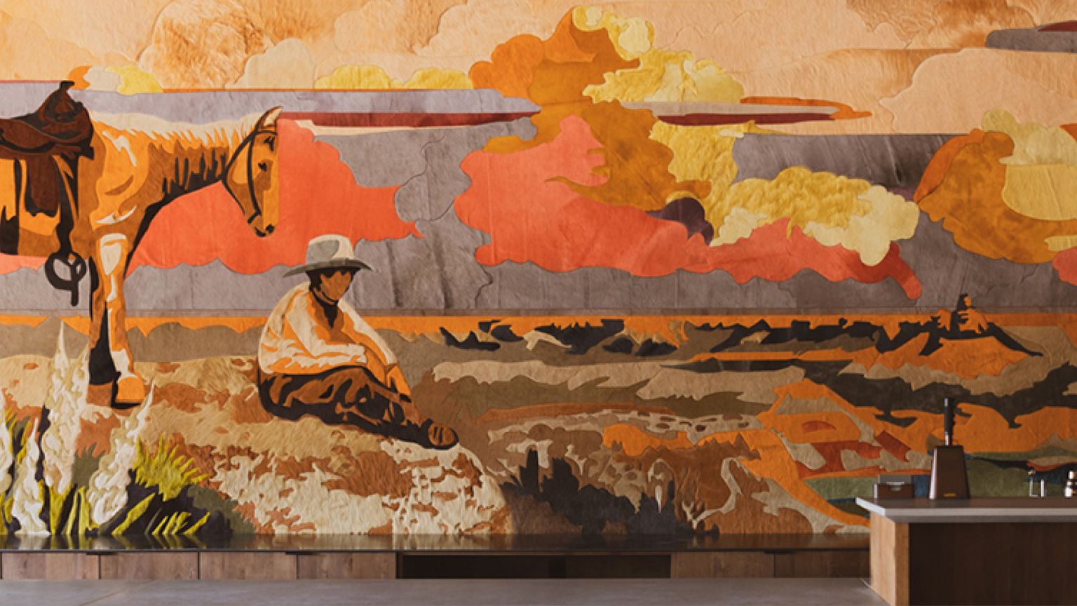 A mural depicts a person in a hat sitting on the ground next to a saddled horse, with a colorful landscape and dramatic sky in the background.