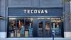 The image shows the word "Tecovas" written in a cursive font on a patchwork background of various shades of brown leather.
