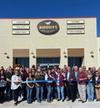 A group of people stands in front of a Murdoch's Ranch & Home Supply store, holding a large ribbon for a ribbon-cutting ceremony.