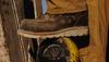 A person wearing a brown work boot and tan pants stands with one foot on a yellow industrial gauge.