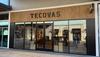 The storefront of Tecovas, a retail store with large glass windows and wooden accents, displaying boots and western apparel inside.