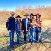 Five people wearing cowboy hats standing outdoors on grass with trees in the background.
