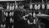 A worker inspects a shoe sole in a factory, with multiple shoe soles hanging on racks in the background.