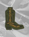 A patch shaped like a cowboy boot reads "Tecovas Official Cobbler" against a grayscale background of boot molds.