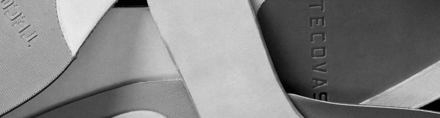 A close-up image of overlapping leather shoe insoles, with the brand name "Tecovas" visible on one of them.