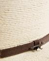 Close-up of a woven straw hat with a brown fabric band and a small metal fox pin attached to the band.
