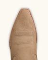 A close-up view of the pointed toe of a tan suede cowboy boot with white decorative stitching and a brown welted sole.