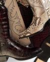 A close-up of overlapping cowboy boots in various textures and patterns, including snakeskin, embossed leather, and stitched designs.