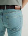 Close-up of a person wearing light blue jeans, a gray shirt, and a brown leather belt with the word "Tecovas" stamped on the belt loop.