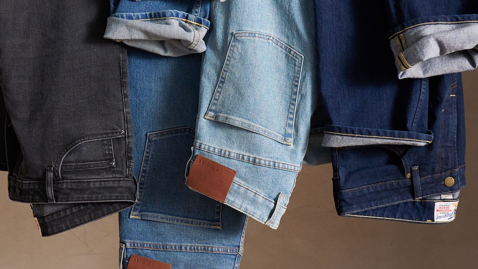 Three denim jackets in different shades of blue are hanging side by side, with visible pockets and stitching details.
