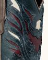 Close-up of a cowboy boot showing detailed stitching and layered leather in dark green, maroon, and cream colors with decorative patterns.