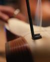 Close-up of a tool branding or burning a mark onto the sole of a leather shoe, with smoke rising and a blurred hand in the background.