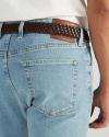 A person wearing light blue jeans with a brown woven belt and a white shirt, shown from the waist down and back view.