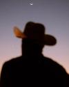 Silhouette of a person wearing a cowboy hat against a twilight sky with a crescent moon and a bright star visible.