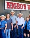 A group of eight people in western attire stand smiling in front of a building with a "NIGRO'S WESTERN" sign.