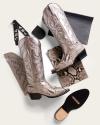 A pair of metallic snakeskin cowboy boots displayed with a snakeskin leather piece, black sole, monogram tags, and a leather swatch on a light background.