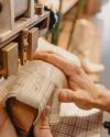 A person holds a light-colored cowboy boot under a machine, likely for stitching or embossing, in a workshop setting.