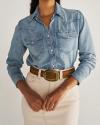 Woman wearing a light denim button-up shirt tucked into a beige skirt with a brown belt featuring a large, rectangular buckle.
