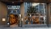 Street view of a Tecovas store with open glass doors, showcasing boots and accessories inside; two people are visible browsing the merchandise.