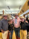 Four people wearing cowboy hats and casual attire are standing together in a western-themed store. Mounted deer heads and shelves with various items are visible in the background.
