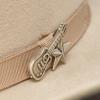 Close-up of a beige cowboy hat with a ribbon band, decorated with a metal lapel pin shaped like a guitar and a star.