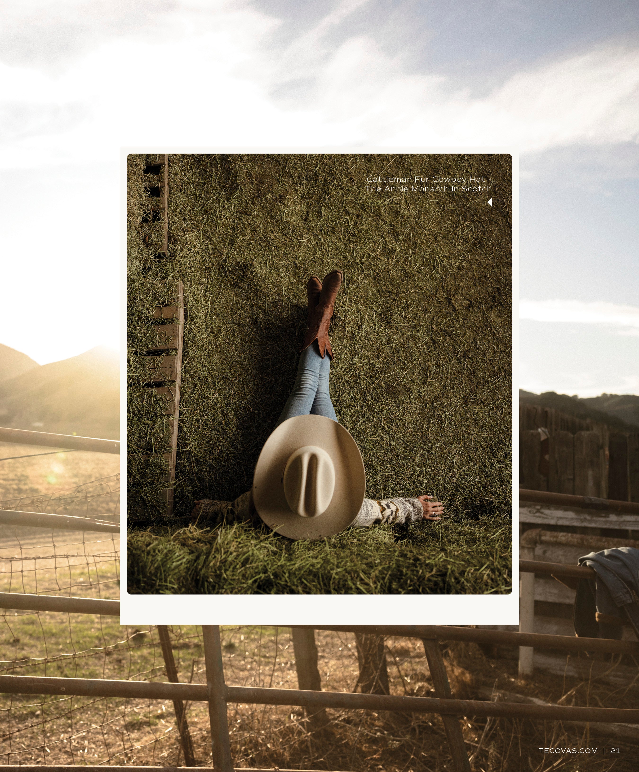 A stylized shot of a person lying on a pile of hay inside a barn, wearing jeans and brown boots (The Annie Monarch in Scotch), with a light-colored cowboy hat resting over their chest. A sunny, rural scene is visible through a fence in the background.