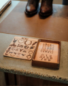 Two wooden boards on a countertop, one with images and symbols, the other with uppercase letters and numbers 0-9.