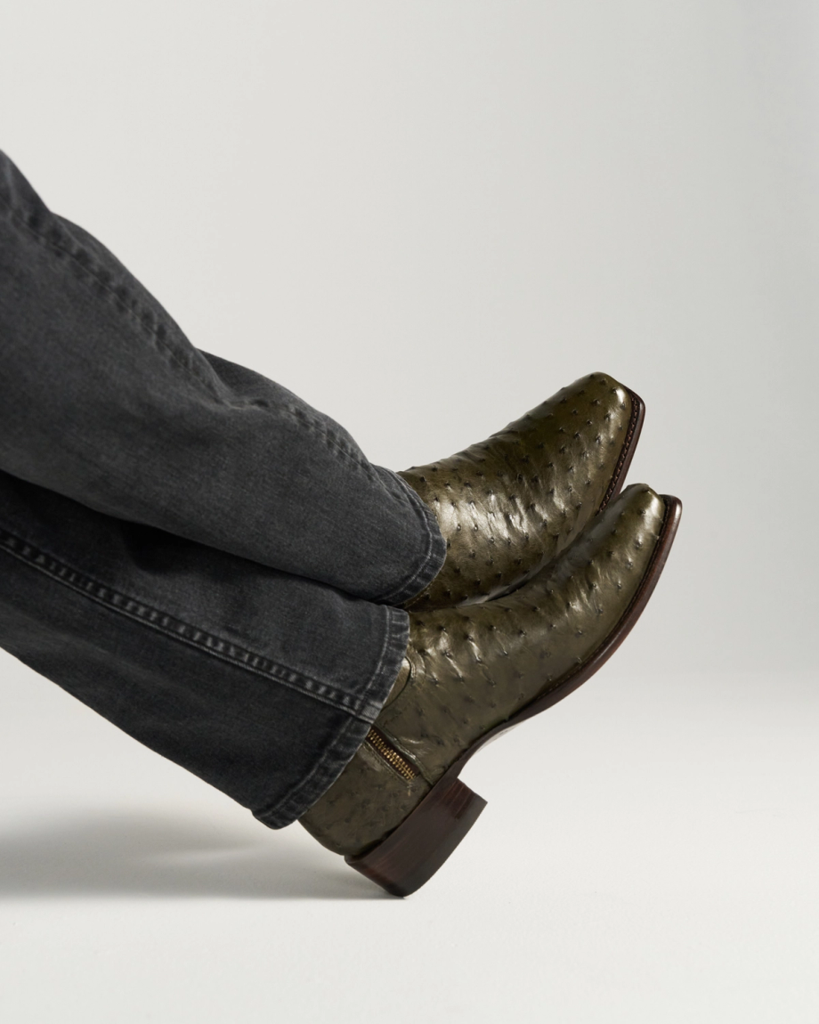 The Jack in Dark Forest Ostrich. A person wearing dark jeans and olive green, textured Dark Forest Ostrich cowboy boots with pointed toes, shown against a plain light background.