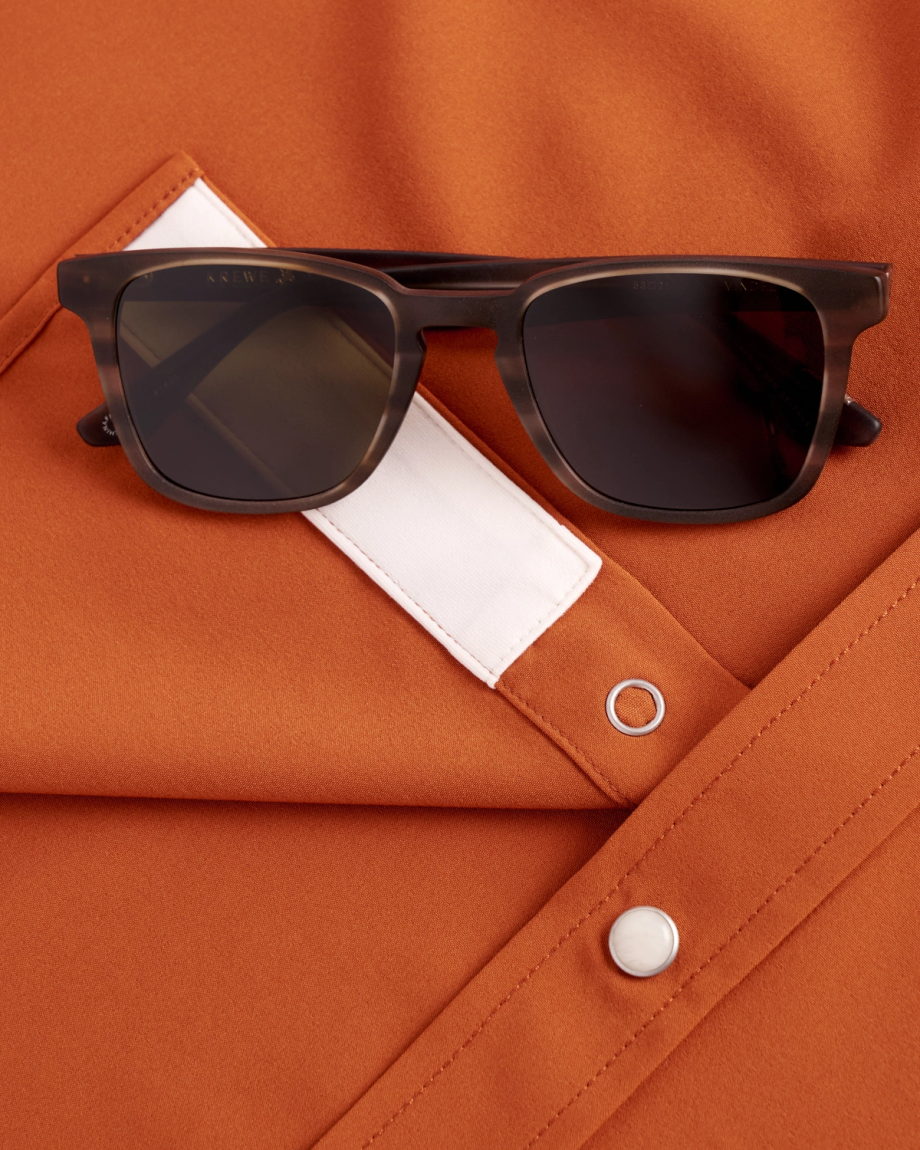 Black sunglasses rest on an orange shirt with a white pocket flap and silver snap buttons.