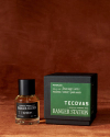 A bottle of Tecovas Ranger Station Waterloo fragrance sits next to its black and green box on a brown surface.